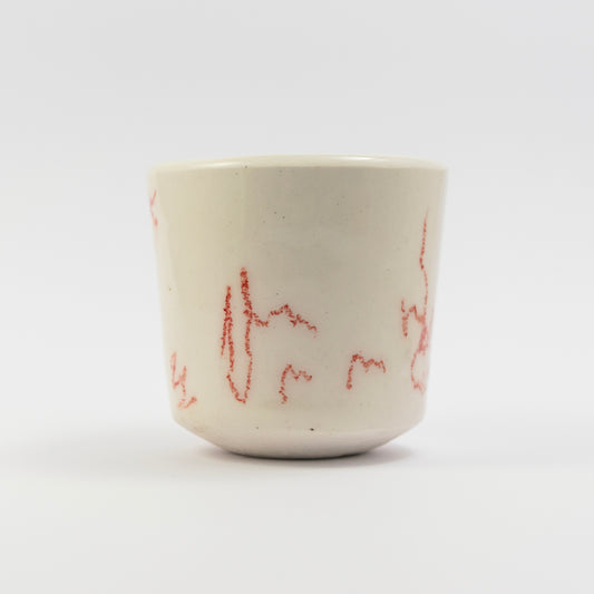 Front view of a porcelain cup with abstract red underglaze pencil scribbles scattered around the surface.