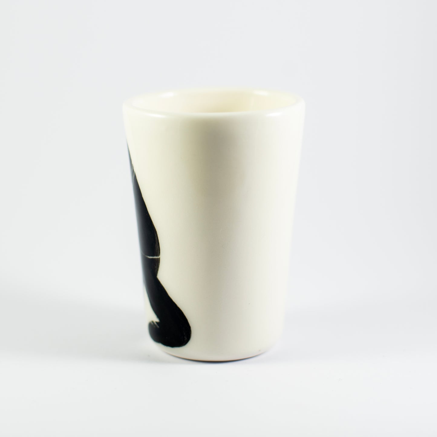 Porcelain cup with a tall, tapered shape and a hand-painted black figure on one side, set against a plain white background.