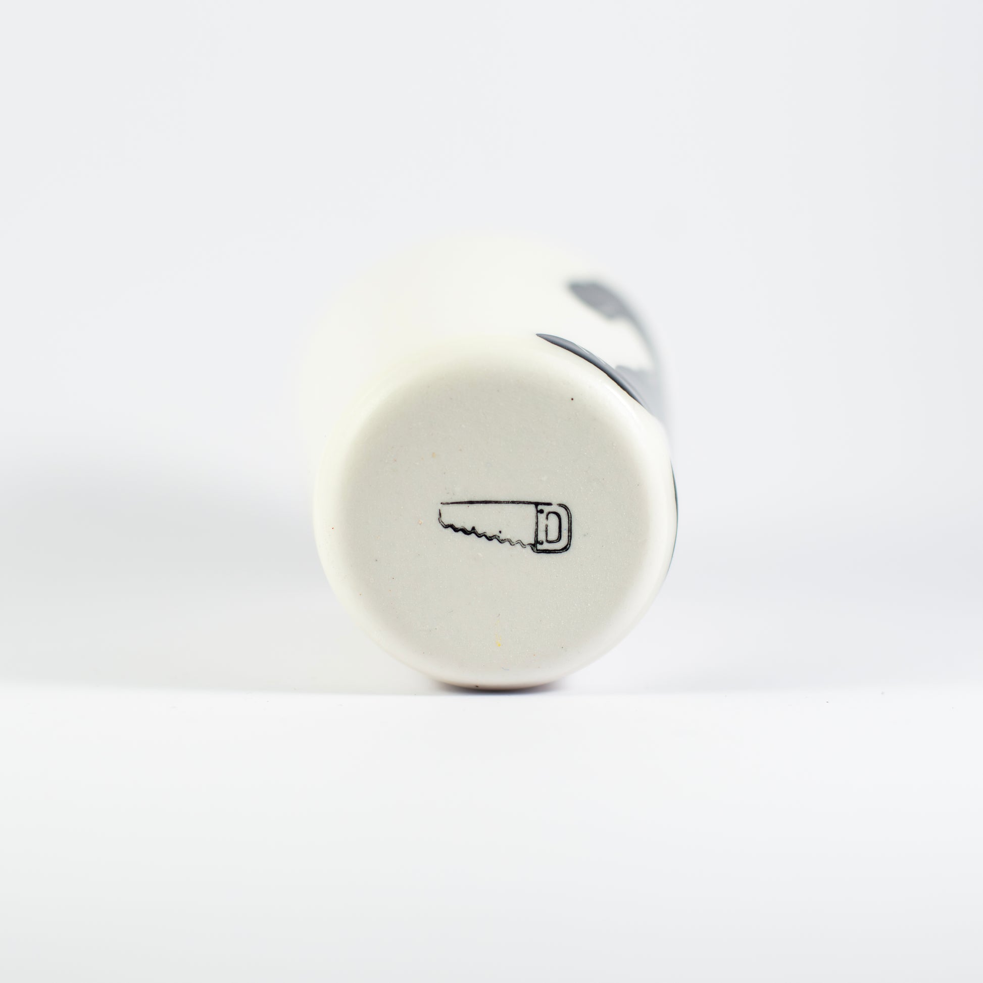Underside of the porcelain cup showing a small black saw logo stamped into the base.