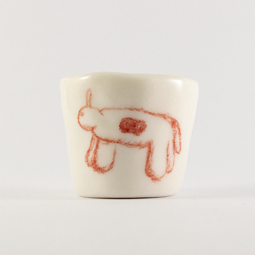 Front view: A ceramic shot glass with hand drawn cartoon horse.
