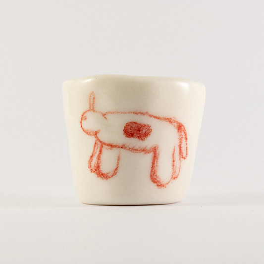 Front view: A ceramic shot glass with hand drawn cartoon horse.