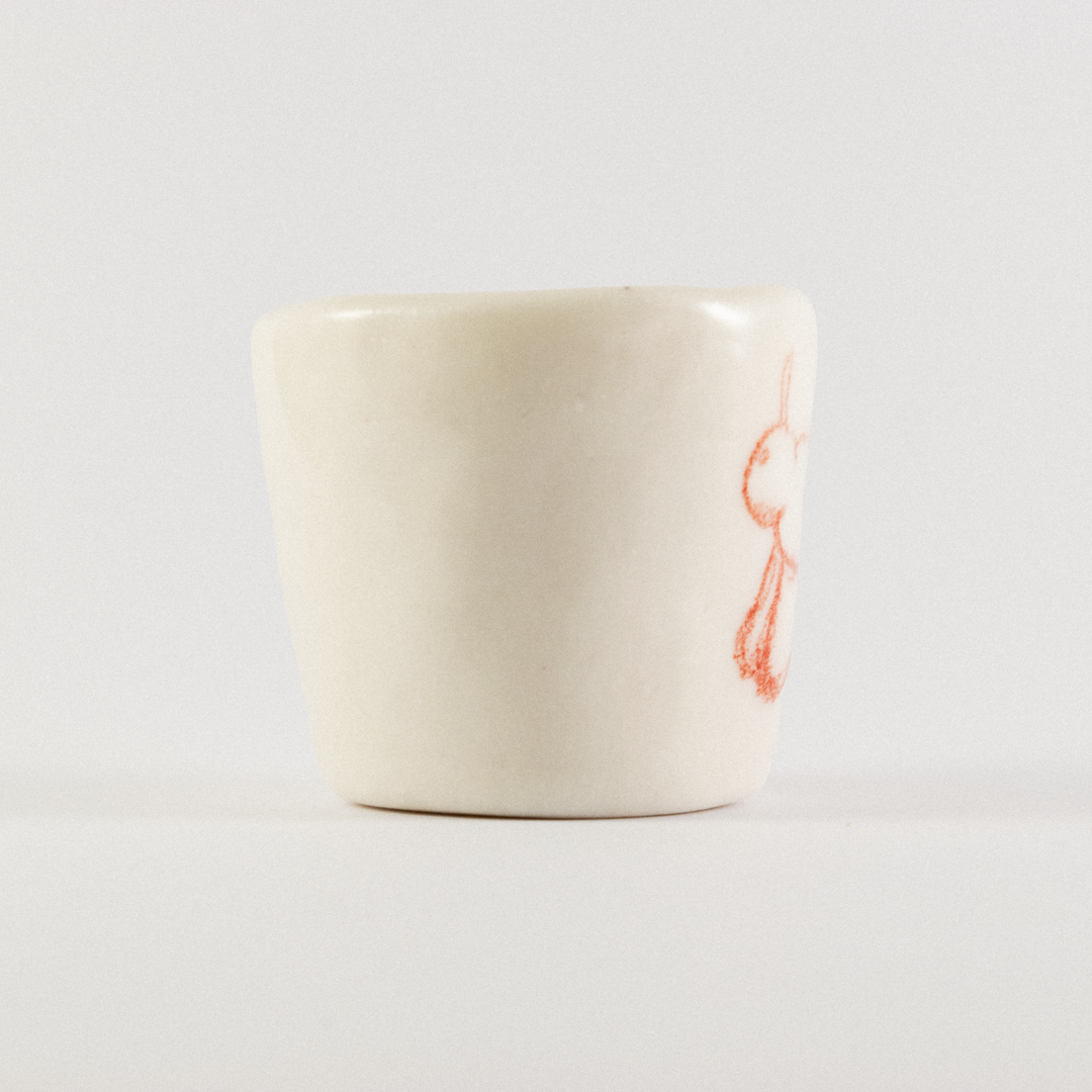 Front view: A ceramic shot glass with hand drawn cartoon horse.
