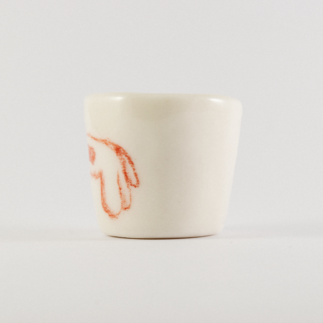 Front view: A ceramic shot glass with hand drawn cartoon horse.