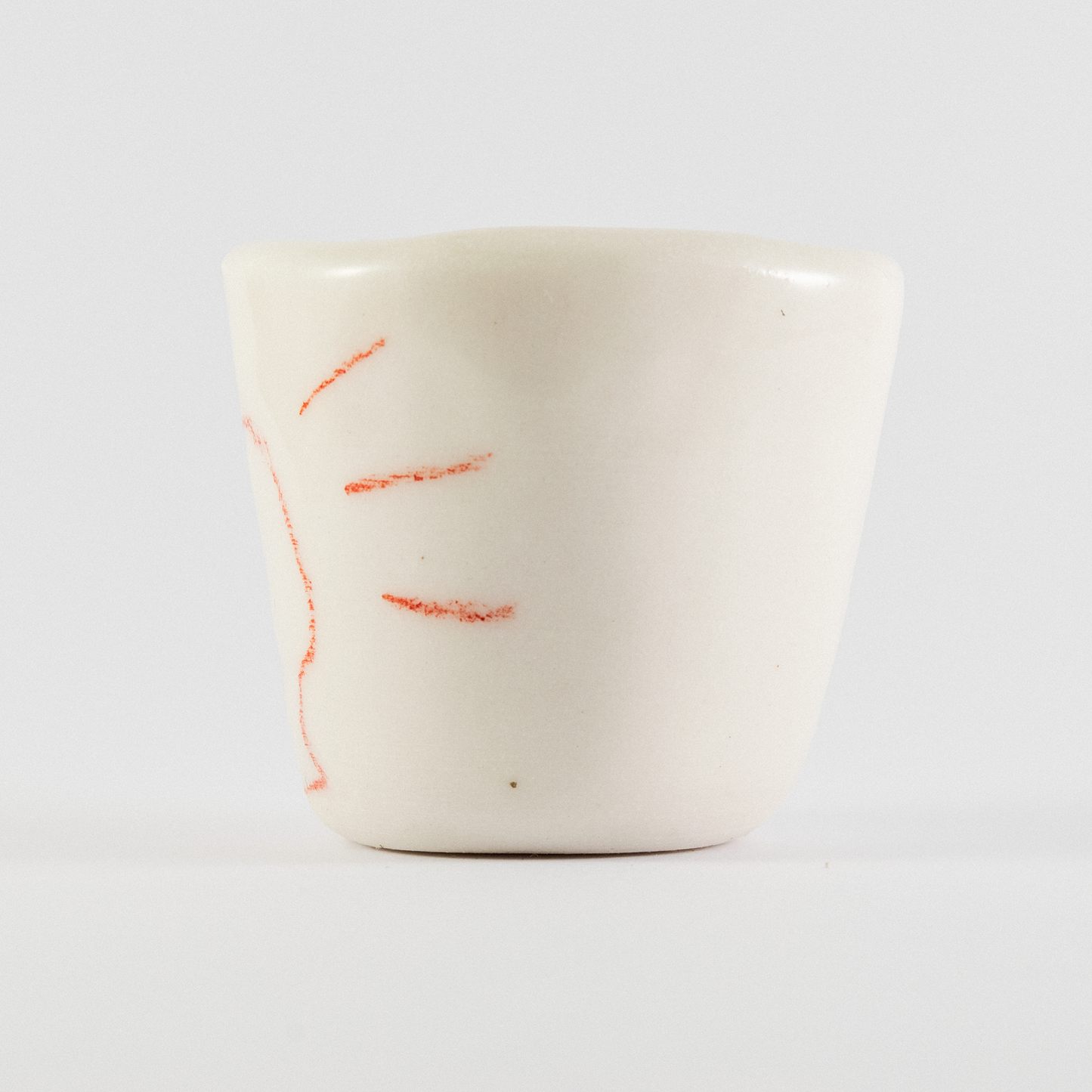 Side view of ceramic shot glass. There is red a hand-drawn doodle of a monster with large spikey teeth.